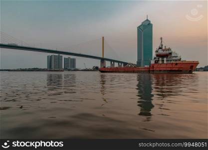 A cargo ship parked in the middle of the Chao Phraya River at evening with Modern building at the background. Selective focus.
