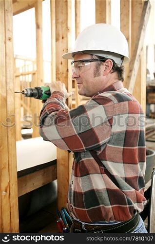 A carpenter on a construction site drilling safely according to safty codes and regulations.
