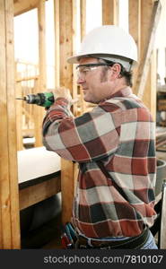 A carpenter on a construction site drilling safely according to safty codes and regulations.