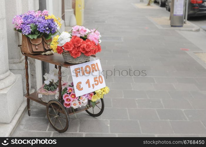 A cart with over wicker baskets and an old wicker fishing basket full of flowers for sale