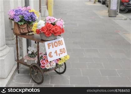 A cart with over wicker baskets and an old wicker fishing basket full of flowers for sale