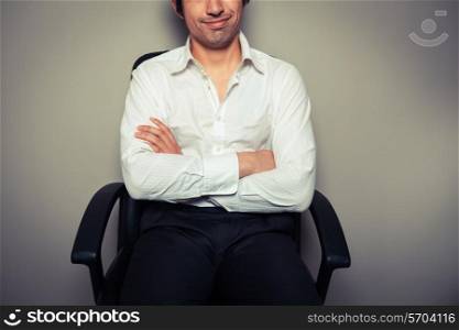 A casual and happy young businessman is sitting in an office chair