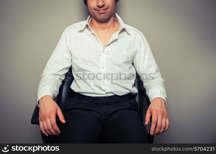 A casual and happy young businessman is sitting in an office chair