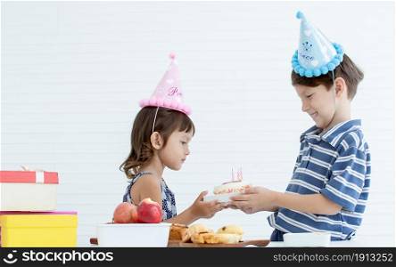 A caucasian boy giving a cake with candle to his little sister for celebrating her birthday