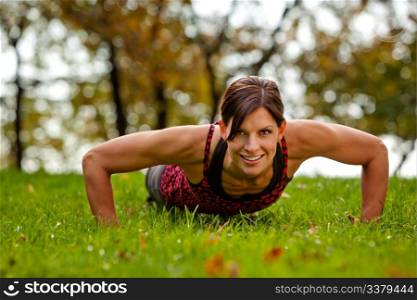 A caucasian female doing push ups in the park