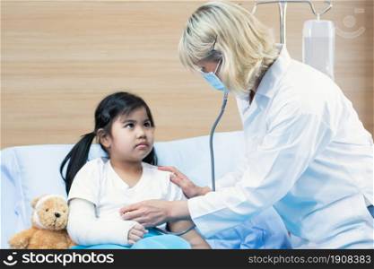 A caucasian female senior doctor is using stethoscope for examining a little girl in room of the hospital. Medical and Insurance Concept.