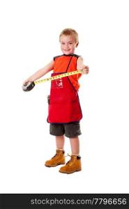 A Caucasian male young child dressed in an orange apron and construction boots holding yellow measuring tape, isolated.