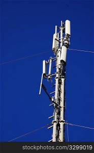 A cell phone antenna tower stands against a deep blue sky