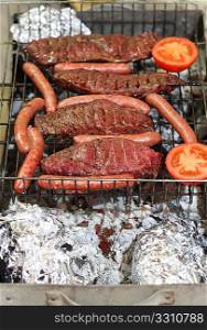 A charcoal barbecue in action, with rump steak, sausages and tomato