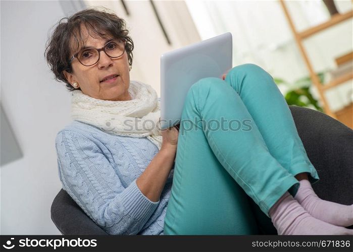 a charming senior brunette woman with glasses using digital tablet at home