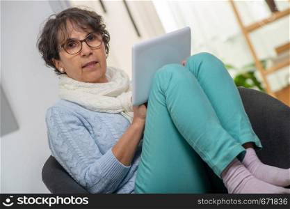 a charming senior brunette woman with glasses using digital tablet at home