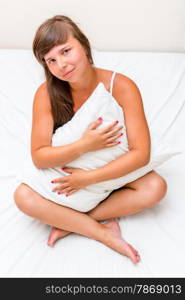 a charming young girl hugging a pillow in bed