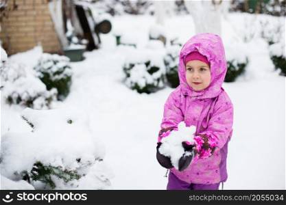 A cheerful child sculpts snowballs outdoors on a winter day. Winter Games.. A cheerful child sculpts snowballs outdoors on a winter day.