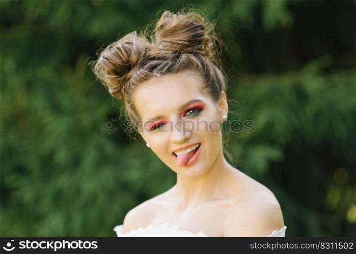 A cheerful funny young woman or girl with bright makeup and a funny hairstyle squinted one eye and shows a smiling tongue