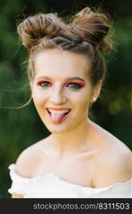 A cheerful funny young woman or girl with bright makeup and a funny hairstyle squinted one eye and shows a smiling tongue