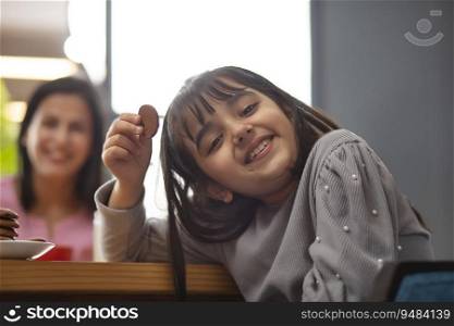 A CHEERFUL YOUNG GIRL LOOKING AT CAMERA WHILE HOLDING BISCUIT IN HAND