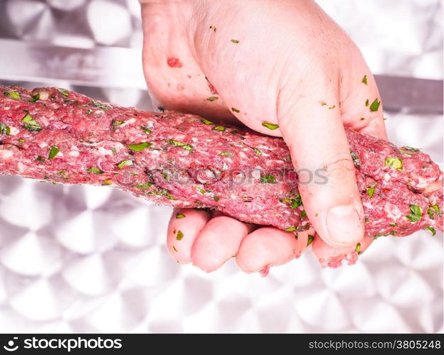 A chef making shish kebab of red meat with parsley over metal plate