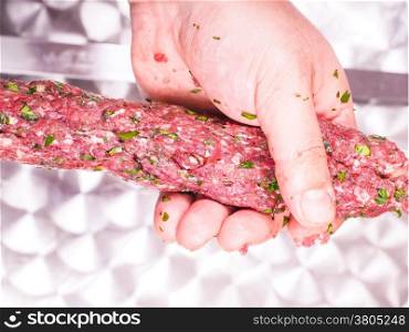 A chef making shish kebab of red meat with parsley over metal plate
