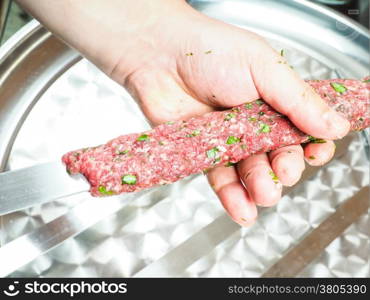 A chef making shish kebab of red meat with parsley over metal plate