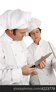 A chef testing the sharpness of his knife blade while a colleague looks on. Focus on male chef.