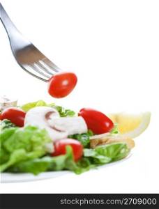 A cherry tomato on a fork above a freshly tossed salad. Shot on white background. Shallow depth of field.