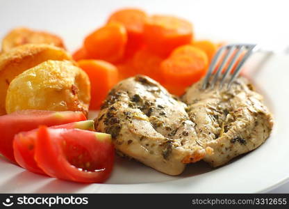 A chicken breast, marinated with oregano and lemon and then baked and served with roast potatoes, boiled carrots and sliced tomato
