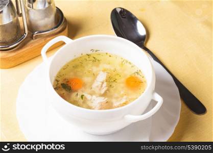 A chicken broth in white ware on the yellow tablecloth