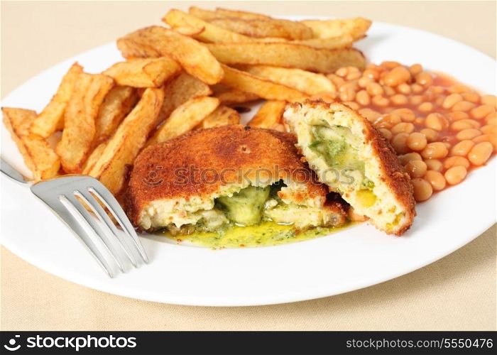 A chicken kiev showing the garlic butter and parsley filling, close-up with baked beans and a fork.
