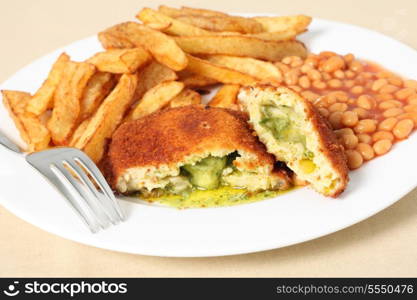 A chicken kiev showing the garlic butter and parsley filling, close-up with baked beans and a fork.