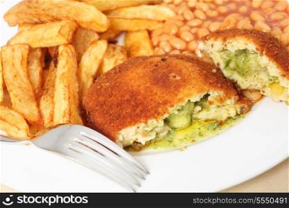 A chicken kiev showing the garlic butter and parsley filling, close-up with baked beans and a fork.