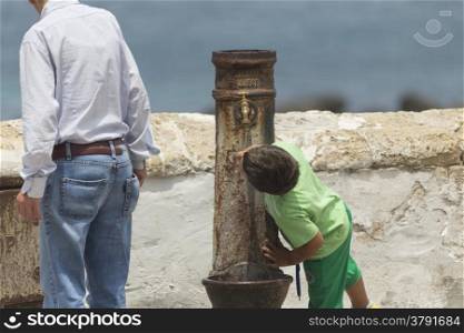 A child drinks water from an old fountain in the old town of Gallipoli (Le) in the southern of Italy