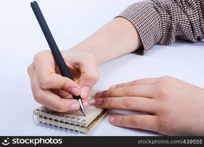 A child hand is writing with pen on a spiral notebook on white background