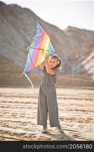 A child is playing with a kite in the sand.. A child launches a rainbow kite 3347.