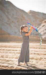 A child is playing with a kite in the sand.. A child launches a rainbow kite 3348.
