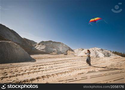 A child launches a rainbow kite.. A child is playing with a kite in the sand 3344.