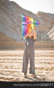 A child launches a rainbow kite.. A child is playing with a kite in the sand 3345.