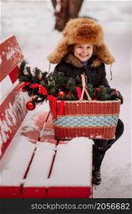 A child with a basket sits on a red bench in winter.. Winter portrait of a child on a bench 3127.