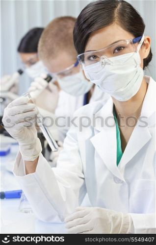 A Chinese Asian female woman medical or scientific researcher or doctor using looking at a test tube of clear liquid in a laboratory with her team