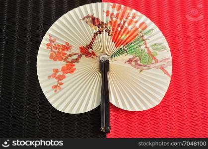 A chinese hand fan isolated on a black and red background