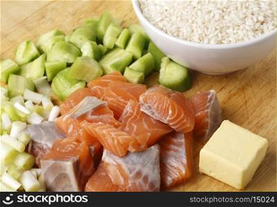 A chopping board with cubed salmon, cucumber, spring onions and butter, ingredients for a salmon risotto