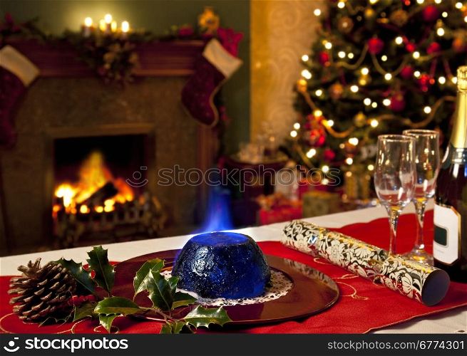 A Christmas Pudding with burning brandy topping with a festive background of fireplace and Christmas tree.