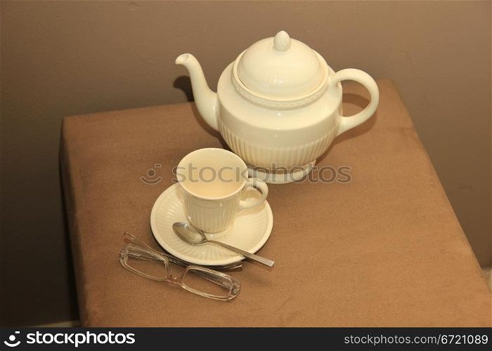 A classic cream white teapot, a cup and a pair of glasses in a still life