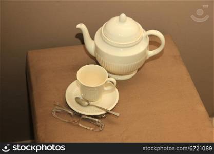 A classic cream white teapot, a cup and a pair of glasses in a still life