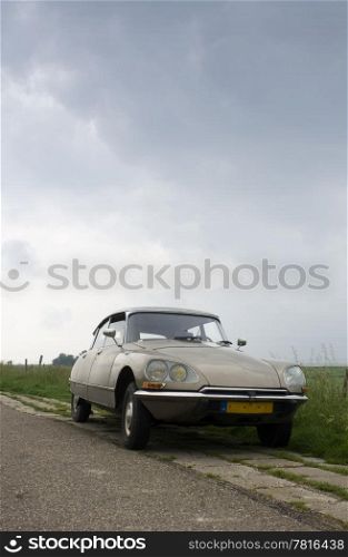 A classic french car parked on the curb of a rural Dutch road on a dyke in Zeeland on a rainy day