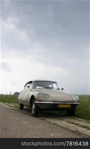 A classic french car parked on the curb of a rural Dutch road on a dyke in Zeeland on a rainy day