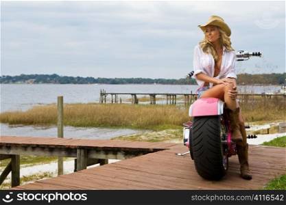 A classic shot of an American blond sitting on a chopper looking out over a lake