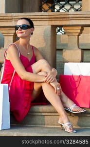 A classically beautiful Mediterranean woman sitting and thinking surrounded by full shopping bags