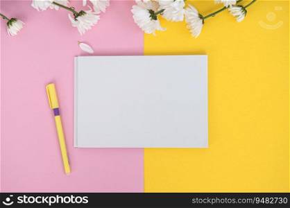 A clean notebook and pen on a light pink table. The concept of business minimalism for women with a bouquet of flowers. Flat plane, top view, place to copy. A clean notebook and pen on a light pink and yellow table. Mockup with a bouquet of flowers