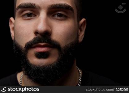 a close-up dramatic portrait of a young serious guy, musician, singer,rapper with a beard and arms crossed on his chest on a black isolated background.