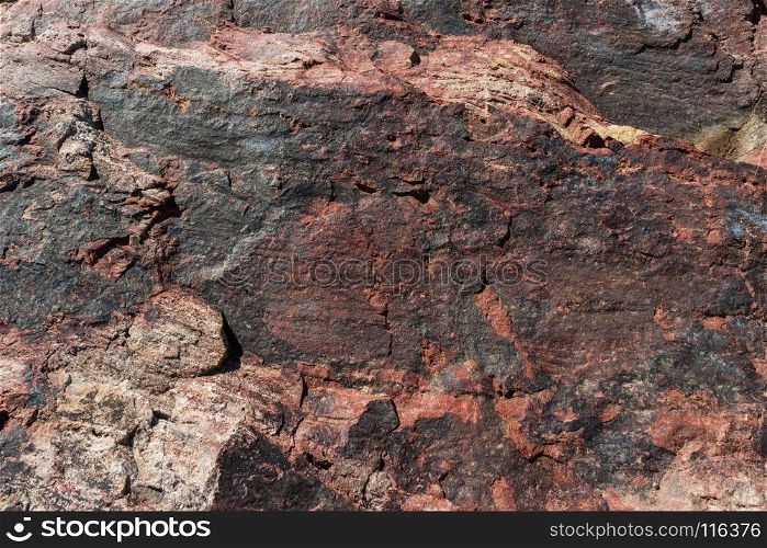 A close-up of a surface of treated rose granite rock plate. A fragment of a stone wall decoration. Texture of deep rose granite facing material